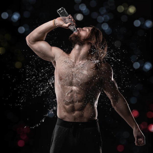 Hombre musculoso atlético bebiendo agua en estudio con salpicaduras