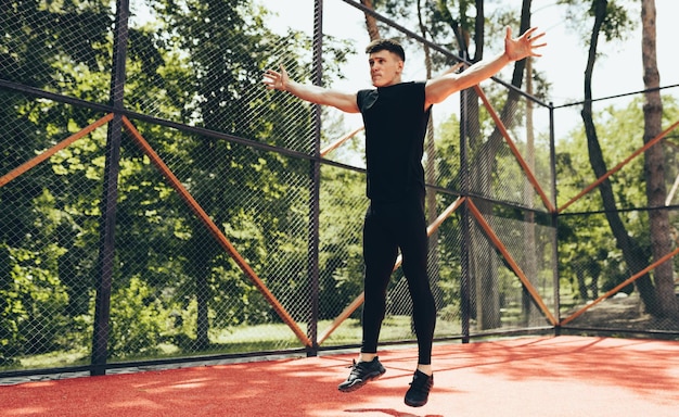 Hombre musculoso atlético joven haciendo ejercicio básico en el campo de deportes Exercis masculino de fitness caucásico haciendo ejercicio en el fondo de la luz del sol Concepto de personas y deporte