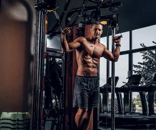 Hombre musculoso atractivo está haciendo ejercicios con aparatos de entrenamiento en el gimnasio.