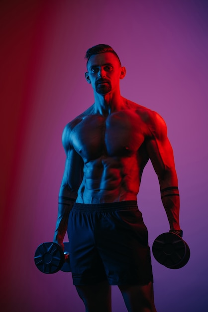 Un hombre musculoso con barba que posa con pesas bajo luces azules y rojas