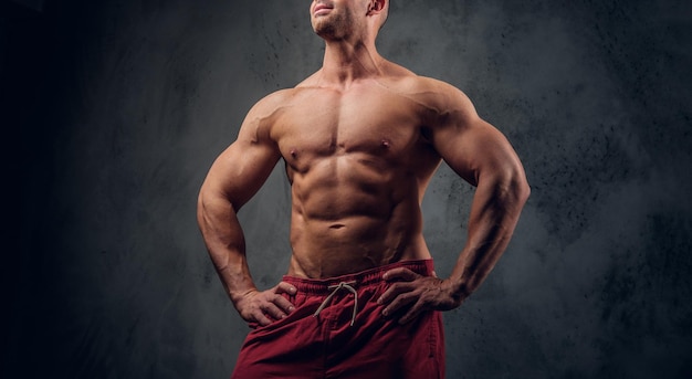 Un hombre musculoso con buenos músculos posa para el fotógrafo en un estudio fotográfico oscuro.