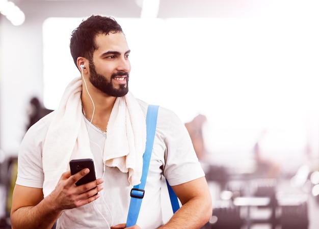Hombre musculoso caminando en el gimnasio con teléfono inteligente