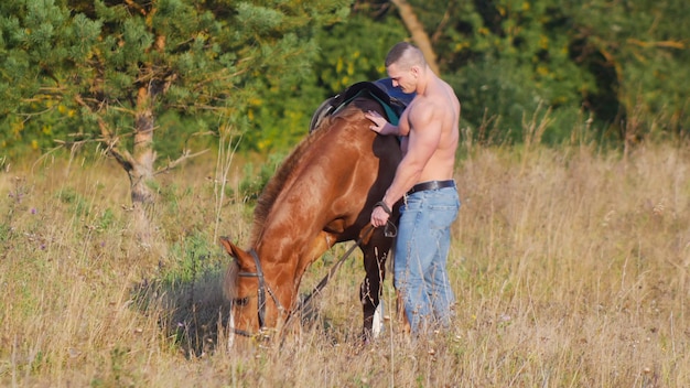 Hombre musculoso sin camisa con un caballo en la naturaleza.