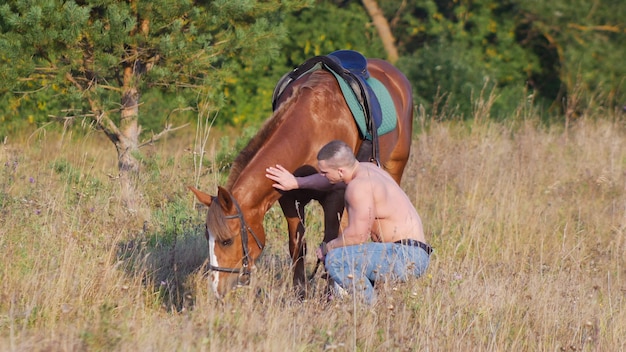 Hombre musculoso sin camisa con un caballo en la naturaleza.