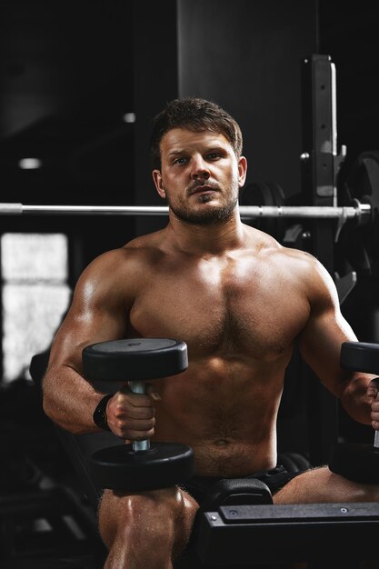 Foto un hombre musculoso sin camisa está haciendo ejercicios de bíceps con ejercicios de pesas como parte de su