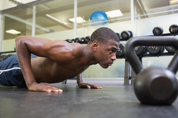 Hombre musculoso sin camisa haciendo flexiones en el gimnasio