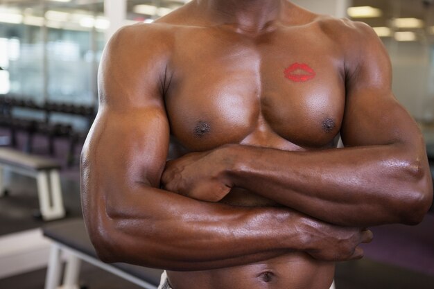 Hombre musculoso sin camisa con marca de lápiz labial en el pecho