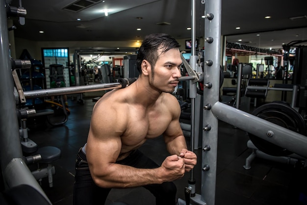 Hombre musculoso sin camisa que dobla los músculos en el gimnasio