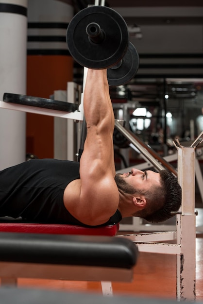 Hombre musculoso ejercitando tríceps con barra