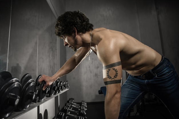 Foto hombre musculoso entrena pesas bíceps en el gimnasio, entrenamiento de manos