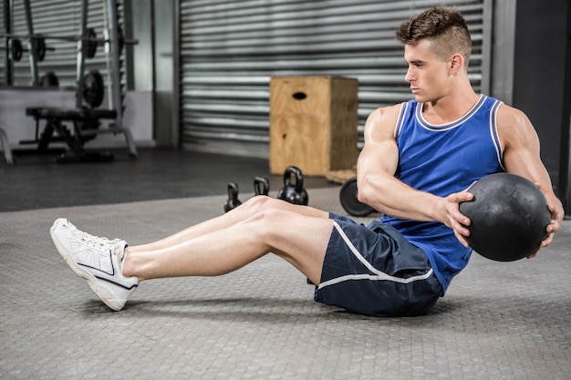 Hombre musculoso entrenando con balón medicinal en el gimnasio de crossfit