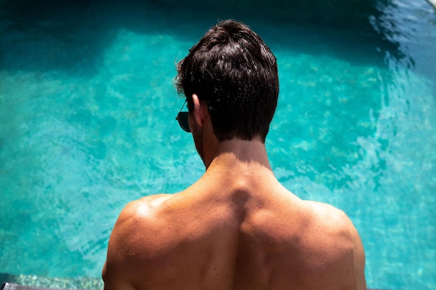 hombre musculoso de espaldas a la cámara mirando a una piscina azul, persona en la piscina