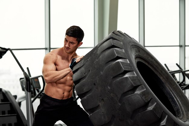 Hombre musculoso fitness volteando la rueda del neumático Concepto entrenamiento funcional gimnasio