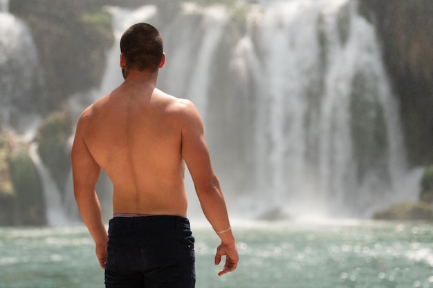 Hombre musculoso flexionando los músculos frente a la cascada