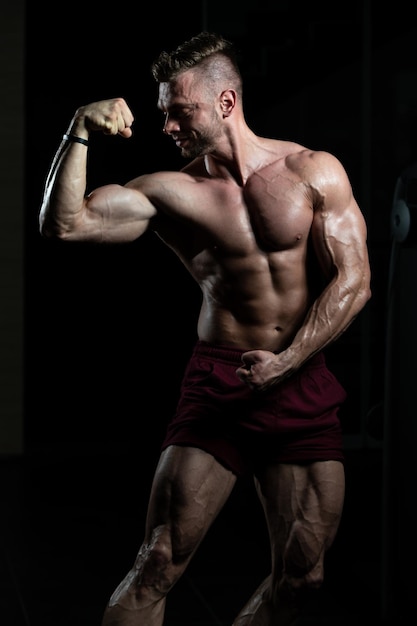 Hombre musculoso flexionando los músculos en el gimnasio