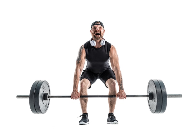 Hombre musculoso fuerte barbudo agresivo en ropa deportiva y auriculares haciendo un ejercicio de peso muerto. Longitud total en blanco.