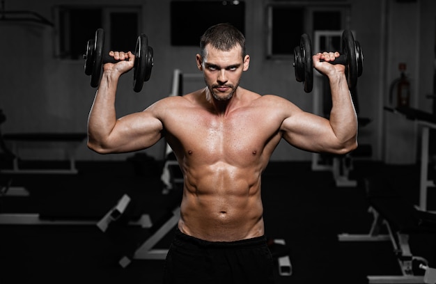 Hombre musculoso en el gimnasio entrenando con mancuernas, el hombre bombea su músculo deltoides