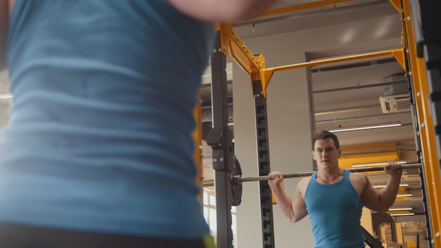 Hombre musculoso de gimnasio fitness realiza sentadillas con barra vista trasera