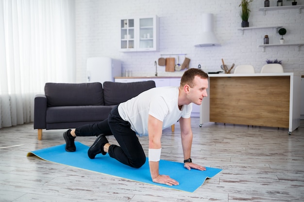 Hombre musculoso guapo con una camiseta está haciendo ejercicios funcionales en el suelo en casa. Fitness en casa. Estilo de vida saludable.