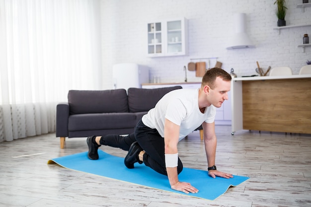 Hombre musculoso guapo con una camiseta está haciendo ejercicios funcionales en el suelo en casa. Fitness en casa. Estilo de vida saludable.