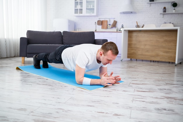 Hombre musculoso guapo con una camiseta haciendo ejercicios de tabla funcional en el suelo en casa. Fitness en casa. Estilo de vida saludable.