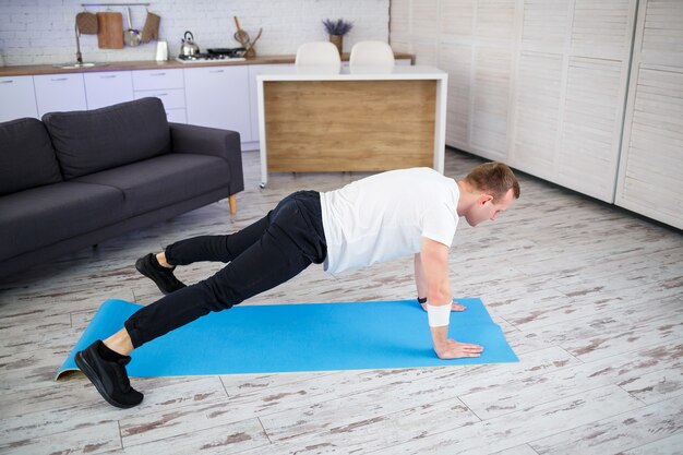 Hombre musculoso guapo con una camiseta haciendo ejercicios de tabla funcional en el suelo en casa. Fitness en casa. Estilo de vida saludable.