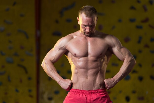 Hombre musculoso guapo flexionando los músculos en el gimnasio