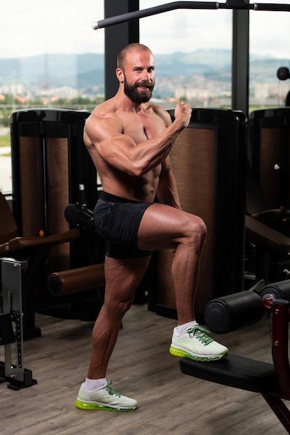 Hombre musculoso guapo flexionando los músculos en el gimnasio