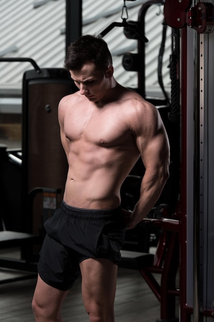 Hombre musculoso guapo flexionando los músculos en el gimnasio