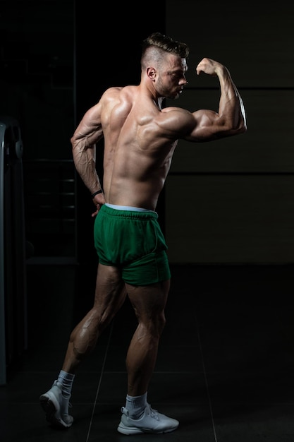 Hombre musculoso guapo flexionando los músculos en el gimnasio