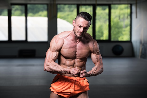 Hombre musculoso guapo flexionando los músculos en el gimnasio