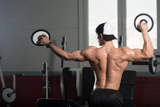 Hombre musculoso guapo flexionando los músculos con pesas