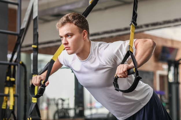 Hombre musculoso guapo haciendo ejercicio con correas TRX en el gimnasio