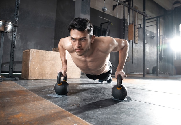 Hombre musculoso guapo haciendo ejercicio de flexión de brazos con mancuernas en un entrenamiento de crossfit.