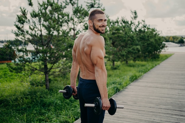 Hombre musculoso guapo con el torso desnudo al aire libre haciendo ejercicios de fitness