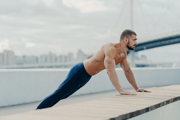 Hombre musculoso guapo con el torso desnudo al aire libre haciendo ejercicios de fitness