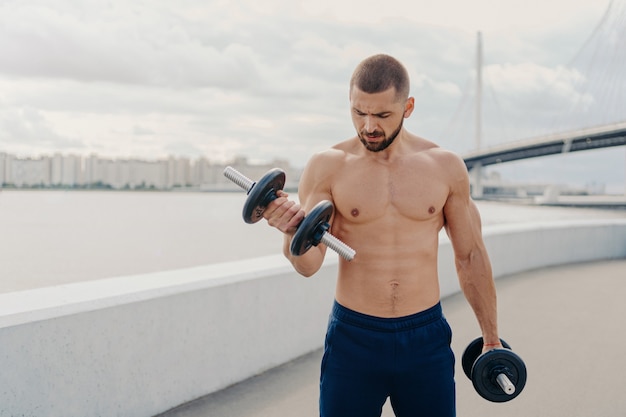 Hombre musculoso guapo con el torso desnudo al aire libre haciendo ejercicios de fitness