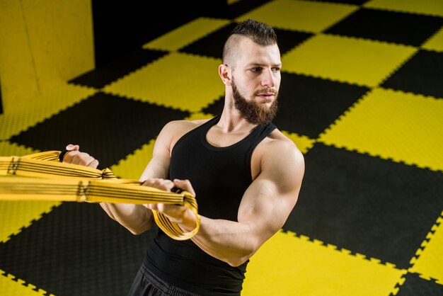 Hombre musculoso hace ejercicios con correas de fitness en el gimnasio con interior negro y amarillo