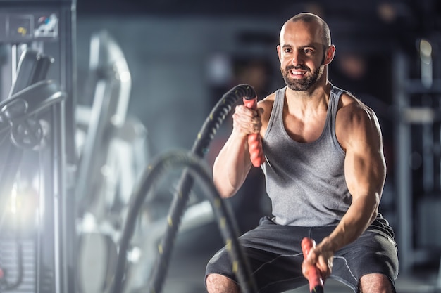 Hombre musculoso haciendo ejercicio con cuerdas de batalla en el gimnasio.