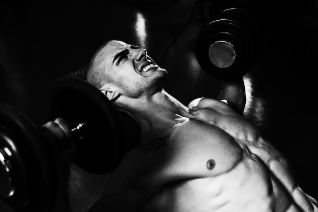 Hombre musculoso haciendo ejercicio para el pecho con pesas en un gimnasio.