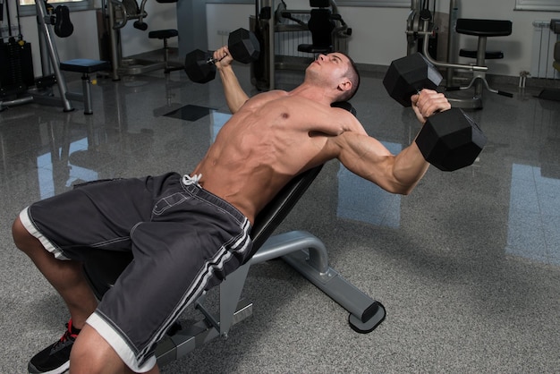 Hombre musculoso haciendo ejercicio para el pecho con pesas