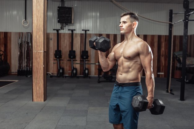 El hombre musculoso está haciendo ejercicio con pesas pesadas, entrenando bíceps en el gimnasio. estilo de vida saludable