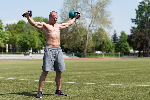 Hombre musculoso haciendo ejercicio con pesas rusas al aire libre