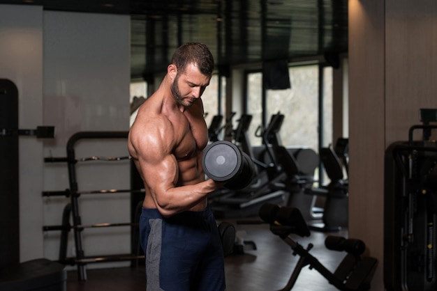 Hombre musculoso haciendo ejercicio de peso pesado para bíceps con pesas en el gimnasio moderno