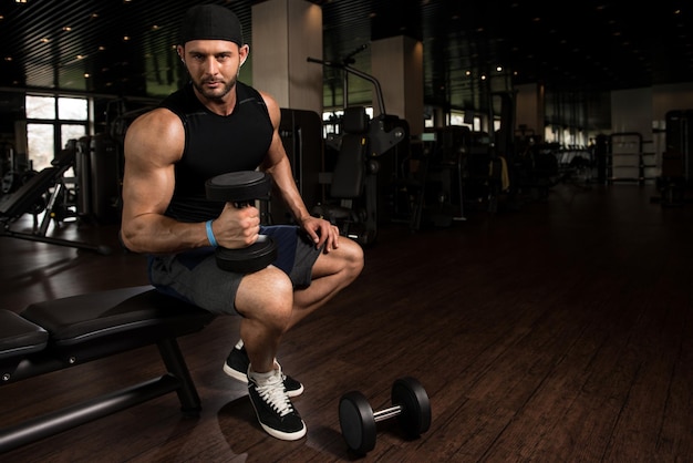 Hombre musculoso haciendo ejercicio de peso pesado para bíceps con pesas en el gimnasio moderno