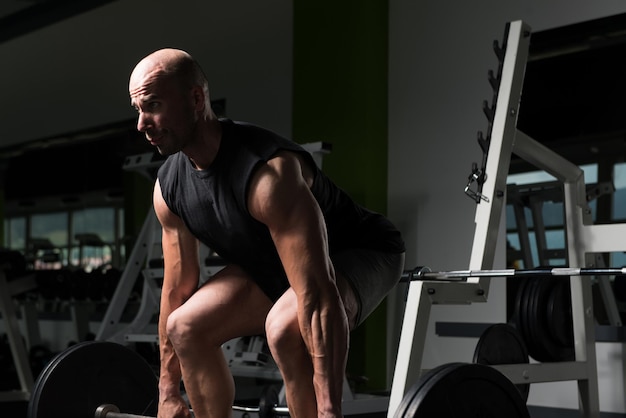 Hombre musculoso haciendo ejercicio de peso pesado para la espalda con pesas en el gimnasio moderno