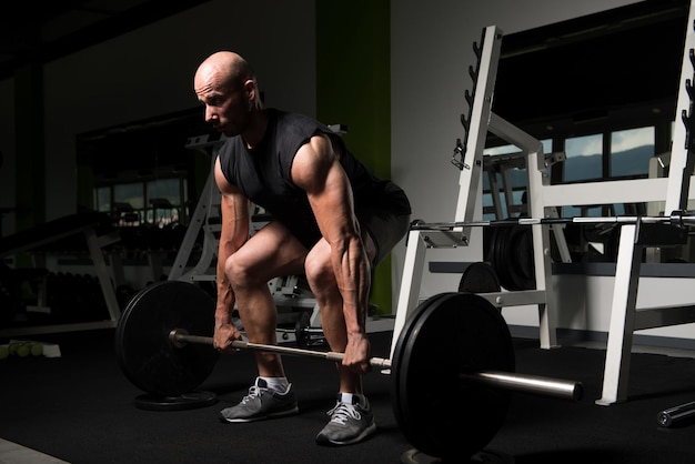 Hombre musculoso haciendo ejercicio de peso pesado para la espalda con pesas en el gimnasio moderno