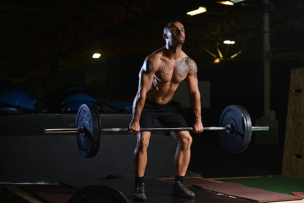 Hombre musculoso haciendo ejercicio de peso pesado para la espalda con pesas en el gimnasio