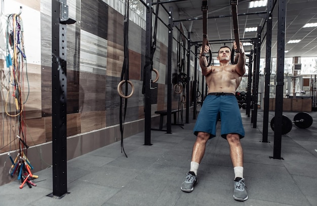 Hombre musculoso haciendo ejercicio con el sistema de resistencia trx en un moderno club de cross-fit. Entrenamiento funcional