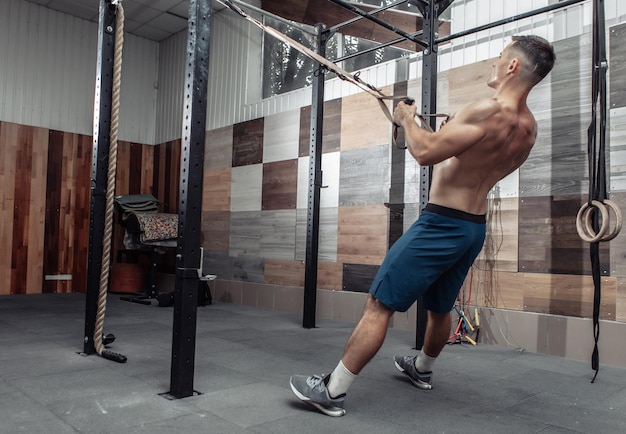 Hombre musculoso haciendo ejercicio con el sistema de resistencia trx en un moderno club de cross-fit. Entrenamiento funcional